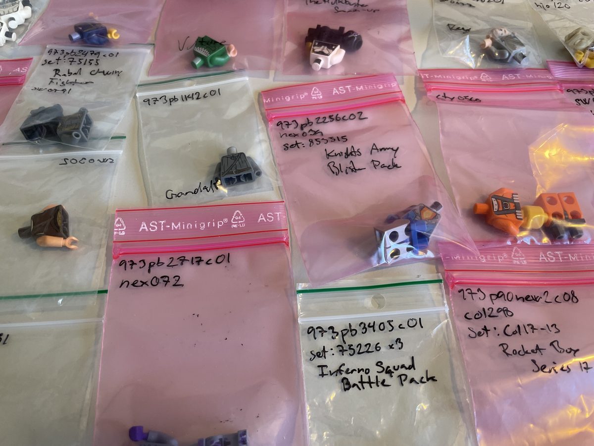 Many small bags of minifigure parts, each hand-labelled with a part number and name